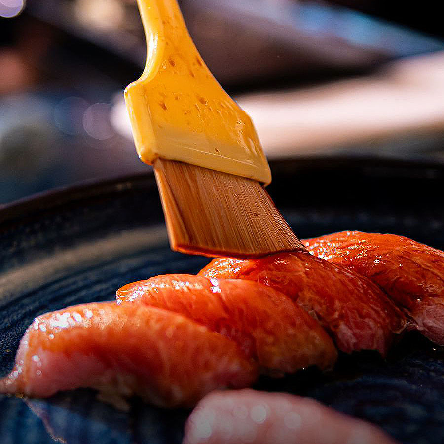 Nigiri flameado siendo pincelado con salsa